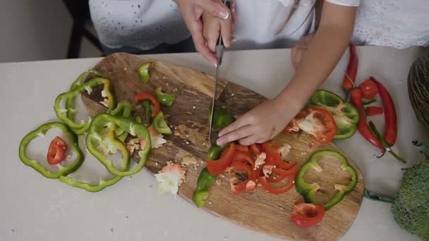 Vista superior. Madre e hija están de pie junto al mostrador de la cocina y cortando pimienta para la preparación de sopa de verduras. Mamá enseña a su hija a cortar verduras y hacer ensalada de verduras — Vídeos de Stock