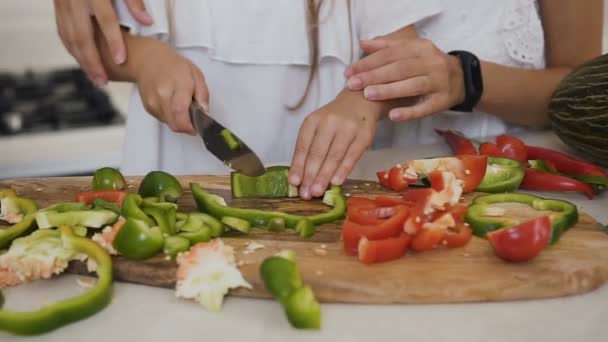 Kızı evde mutfakta sebze kesme öğretim anne. Kızlar bir salata yapmak için kırmızı ve yeşil biber keser. Tasasız küçük kız annesi ile birlikte işlem pişirme ilgilenmektedir — Stok video