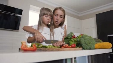 Beyaz elbiseler içinde iki kız evde mutfakta sebze kesiyorsun. İki sevimli kız salata hazırlanıyor. Sağlıklı vejetaryen salata birlikte mutfakta yemek çekici genç kız