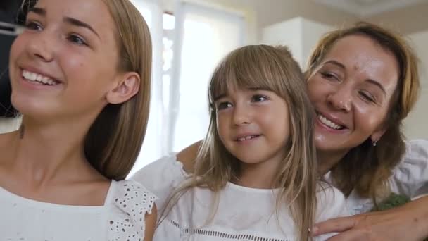 Porträtt av en lycklig familj som gör en selfie, fotograferad på en smartphone medan matlagning i köket. Mamma och hennes döttrar är klädd i vita kläder, laga grönsakssallad och ha kul fotograferade — Stockvideo