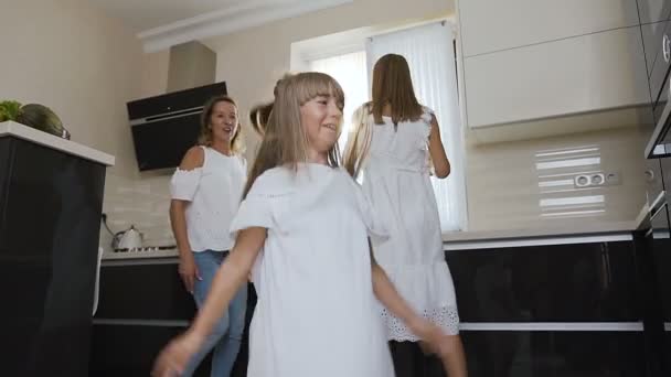 Feliz niña con su hermana y mamá en ropa blanca están bailando y escuchar música mientras se cocina en la cocina en casa. Familia feliz — Vídeos de Stock