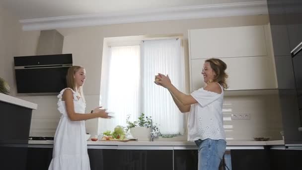 De belles filles en vêtements blancs s'amusent tout en se jetant une grosse pomme verte à la maison dans la cuisine. Maman et deux filles jouent à un jeu amusant avec la pomme dans la cuisine de la maison. Heureux — Video