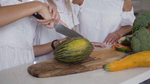 Primer plano de una mujer manos cortando melón fresco con cuchillo y tabla de cortar de madera en la cocina en casa. Corte de melón verde, melón sobre tabla de madera — Vídeo de stock