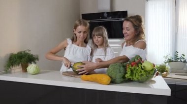 Anne ve kızları yemek mutfakta iki: kadın yeşil kavun kesmek için kızları öğretir. Anne ve iki kız şirin aile hazırlamak vejetaryen salata evde mutfakta