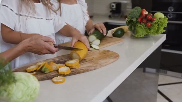 Het vrouwtje handen snijden courgette met een mes. Donker groene en gele courgette opleggen van een snijplank in een keuken. Twee meisjes groene en gele courgette op het bord is snijden met een mes op de — Stockvideo