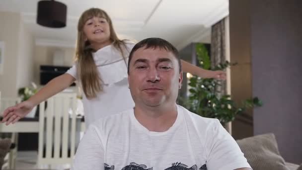 Närbild av glada teen flicka med långt hår kramar hennes pappa och skrattar i vardagsrummet hemma. Far och hans vackra dotter. Lycklig familj — Stockvideo