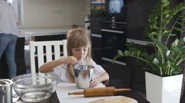 Yakın çekim küçük kız annesini mutfakta meşgul ise hamur pişerken kaşık ile un karıştırma. Kurabiye pişirmeye annesi yardım küçük güzel kız