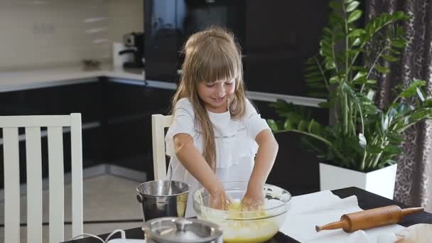 Mosoly kislány dagasztás egy tésztát l-egy nagy pohár, tál, a konyhában. Boldog kis lány a konyhában. A gyermek készül a tészta, sült a cookie-k — Stock videók