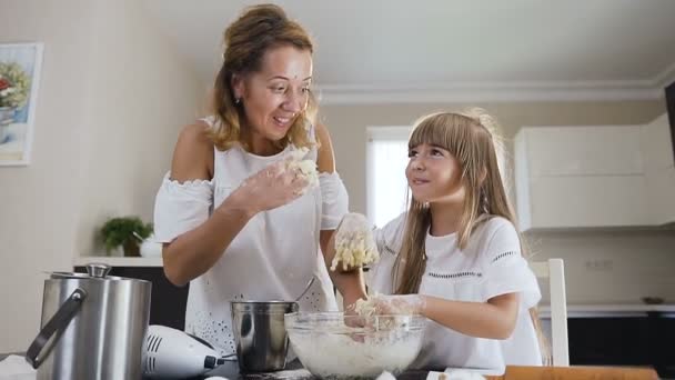 Close-up of the cute little girl and her young mother having hands in dough because they kneading it and taste it. Happy mom with daughter. Bake cookies — Stock Video