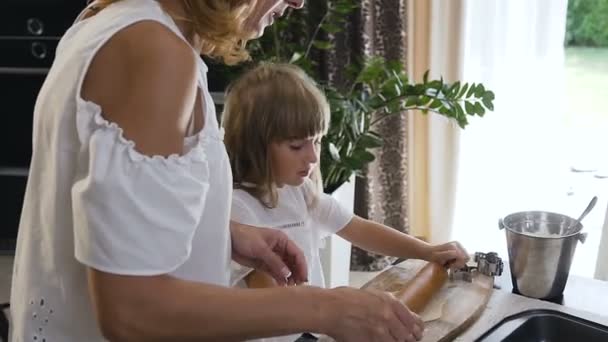 Primer plano de una hermosa madre enseñando a su hija a cocinar y amasar una masa para galletas en la mesa de la cocina en casa. Hornear galletas en casa — Vídeos de Stock