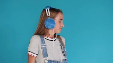 Portre. Dans ve müzik kulaklık ritim dinlemek için hareketli sevimli kız. Mavi arka plan. Kulaklıklar giyen genç kız