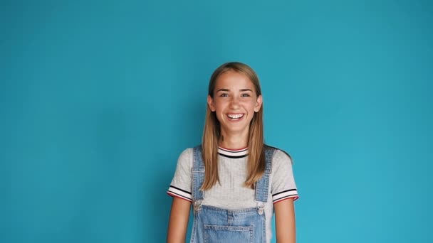 Gelukkig lachend Kaukasische jong meisje. Portret van schattige tiener meisje met lang haar glimlachend in de camera op een blauwe achtergrond. Close-up, portret van aantrekkelijk meisje lacht zelfverzekerd en mooi — Stockvideo