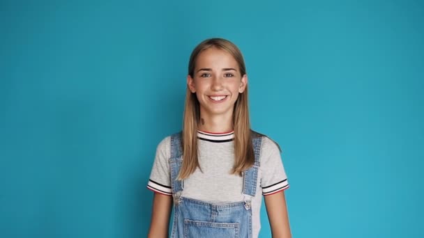 Close up de bela menina branca olha e aponta para o polegar da câmera para cima. Retrato de uma menina da escola americana bonito é alegre sorrindo e levantando o polegar. Conceito de sucesso e aprovação, ok gesto — Vídeo de Stock