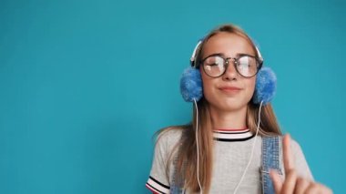 Dans ve ritim dinleme müzik mavi arka plan, Kapalı kulaklıklar hareketli sevimli genç kız. Gülümseyen ve kulaklık müzik dinlemek Gözlüklü kız. Güzel bir portresi