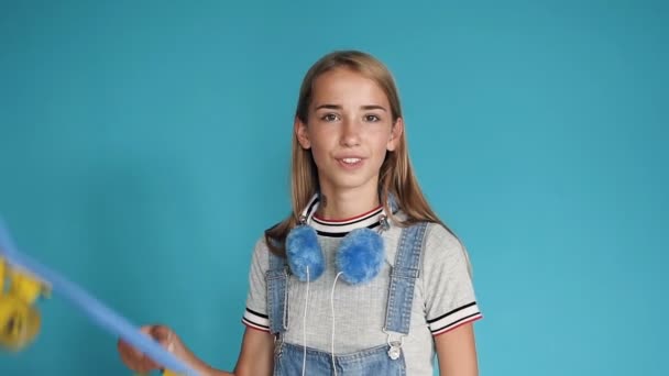 Retrato de uma menina adolescente com skate em seu ombro no fundo azul. Tempo livre de adolescentes. Atividades de lazer e esporte. Menina adolescente bonita feliz segurando skate em seus ombros e — Vídeo de Stock