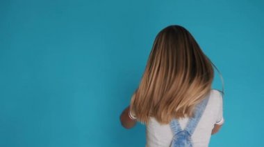 Kendini mavi arka plan üzerinde iplik uzun sağlıklı saçlı güzel kız. Mavi arka plan üzerinde izole başını sallayarak uzun saçlı Sevimli gülümseyen kız