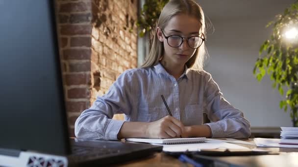 Jovem caucasiana feliz usando computador tablet no escritório moderno. Estudante escrevendo um relatório sobre marketing de sucesso. Belo trabalhador de escritório olhando para o monitor de tela e escrevendo algo em — Vídeo de Stock