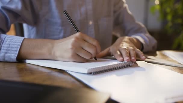 Young girl working with documents and laptop in modern office. A womans hand writing down on a white blank notebook on table in office. Busy business young woman reviewing reports — Stock Video