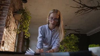 Gözlük takan ve modern ofiste zaman akşam adlı çalışma güzel genç iş kadını. Güzel iş kadını ofiste dizüstü bilgisayar ile masada notlar yapma konsantre
