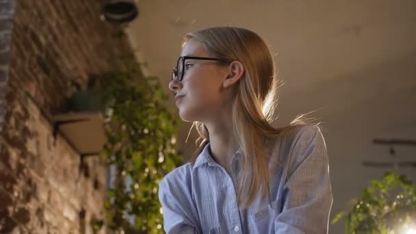 Hermosa chica con gafas con el pelo largo está trabajando en la noche en la oficina moderna. Mujer de negocios hermosa concentrada haciendo notas en la mesa con el ordenador portátil en la oficina — Vídeo de stock