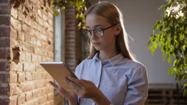 Estudio, negocios, personas, finanzas y concepto contable. Hermosa mujer joven con el pelo largo en gafas trabaja en la tableta que sostiene la tableta en la mano. Joven empresaria que trabaja con la tableta en moderno — Vídeos de Stock