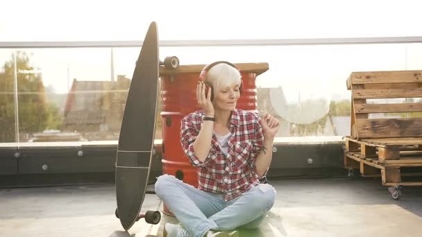 Blonde girl having fun and listening to the music with headphones. Handsome young woman with blonde hair feeling happy dancing on a rooftop listening to music in headphones — Stock Video