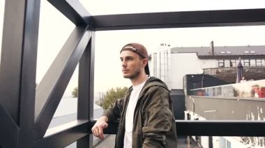 Yakışıklı adam endüstriyel inşaat manzaralı rai merdivenlerde duruyor. Genç hipster adam kameraya bakarak bina endüstriyel merdivenlerde ayakta