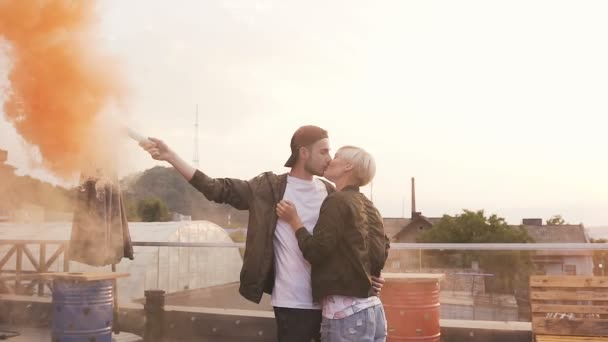 Schöner Hipster-Typ, der seine glückliche Freundin romantisch küsst. schöner junger Mann mit farbigem Rauch und küsst seine Freundin bei Sonnenuntergang auf der Terrasse. Konzept von Liebe und Küssen — Stockvideo