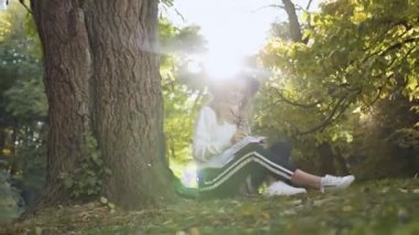 Bazıları onun defterine Not yapar iken parkta ağaç yakınındaki oturan kadın gülümsüyor. 4k