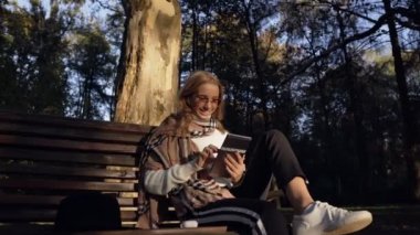 Müzik dinleme ve yeşil parkta bankta otururken tablet kullanarak genç ve güzel kadın.