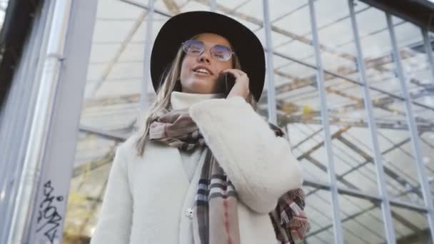 Mujer joven con estilo en el sombrero hablando con alguien en el teléfono móvil al caminar en el parque . — Vídeo de stock