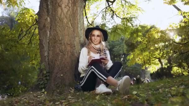 Hermosa Mujer Joven Sombrero Gafas Sol Sentado Cerca Del Árbol — Vídeo de stock