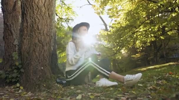 Jeune femme réfléchie prenant note dans son carnet de notes tout en s'asseyant sur l'herbe gteen dans le parc de la ville . — Video