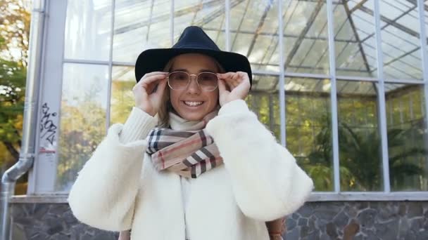 Mulher branca bonita em chapéu elegante olhando para a câmera e vestindo óculos de sol no parque. Fechar tiro . — Vídeo de Stock