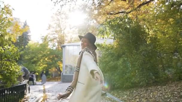 白いコートとファッション スカーフ ジャンプし 回転し 太陽の光と緑豊かな公園を歩きながら笑って幸せなかわいい若い女 — ストック動画