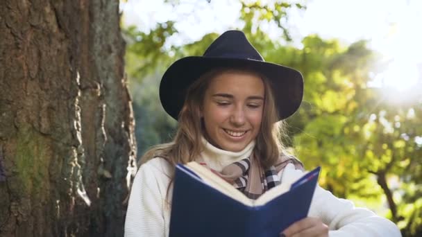 Mooie jonge vrouw in zwarte hoed lezen boek op het groene park-achtergrond. — Stockvideo