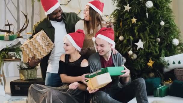 Jovens engraçados estão compartilhando presentes com decorações de Natal e uma bela árvore de Natal. Celebração de Ano Novo de meninos e meninas bonitos e sorridentes. Conceito de Natal e Ano Novo . — Vídeo de Stock