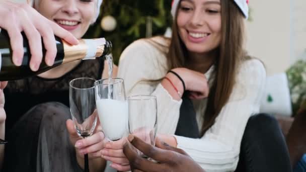 Nahaufnahme. Sekt wird in ein Glas gegossen. schöne Mädchen und Jungen verschiedener Rassen, halten Weingläser mit Weißwein in der Hand und feiern freudig Weihnachten und Neujahr. Weihnachtsdekoration — Stockvideo