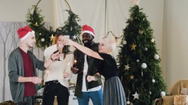genel planı. şık genç insanlar kutlamak Noel ve yeni yıl güzel bir odada Noel ağacı ve dekorasyon. Arkadaşlar sevinçle bir kadeh şampanya yukarı kaldır ve Bengal ışıkları yakmak