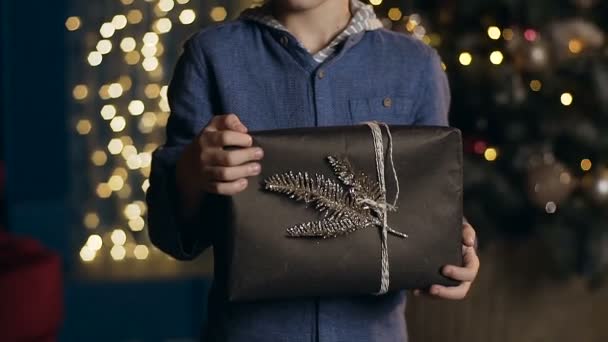 Pequeño niño lindo en camisa azul sosteniendo regalo de Navidad en la mano . — Vídeos de Stock