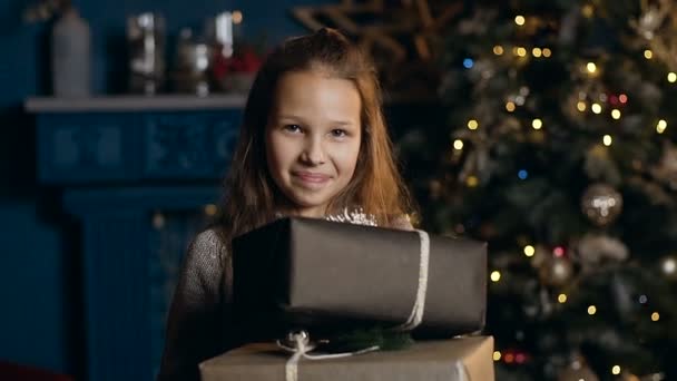 Retrato de niña hermosa sosteniendo dos presente y sonriendo en la cámara en la habitación con árbol de Navidad . — Vídeos de Stock