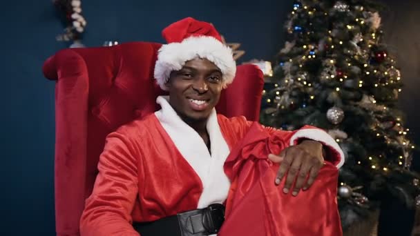 Close up shot of santa claus in the red hat holding the gift box and smiling to the camera. — Stock Video