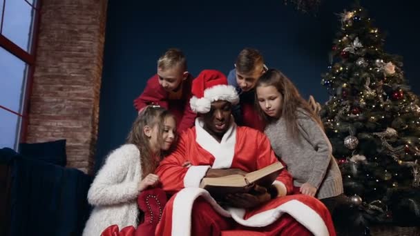 Mignon Père Noël claus dans drôle chapeau livre de lecture avec les enfants . — Video