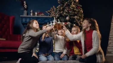 Şirin beş çocuk alkış Noel ağacı arka planda rahat oda çay fincan.