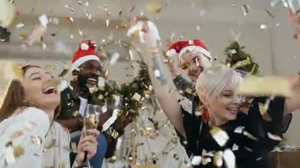 Happy mladých lidí ve slavnostních šatech se sklenkami vína se usmívající se a tančí v létání zlaté konfety na nový rok nebo vánoční večírek. Multi rasové skupiny funny lidé slaví strana