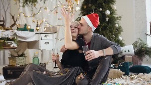 Genç çift Noel ve yeni yıl birlikte, onlar katta oturan ev Noel süslemeleri ve Noel ağacının yakınında şarap içme kutluyoruz — Stok video
