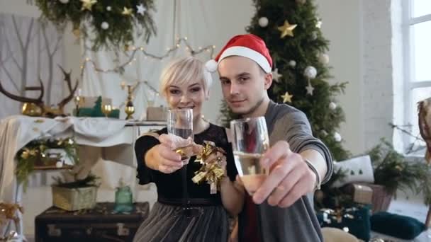 幸福的年轻夫妇正在庆祝新年或圣诞节喝烤面包, 在家里的圣诞树背景咯咯眼镜。节日、家庭和庆祝活动的概念 — 图库视频影像
