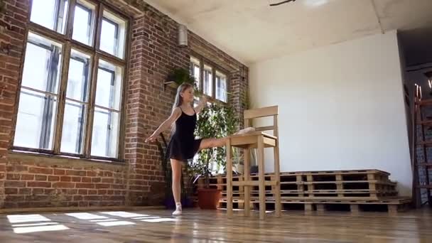 Holka dělá strečink v tanečním sále. Atraktivní dívka v černém tutu se zabývá baletu. Gymnastka dívka dělat warm-up — Stock video