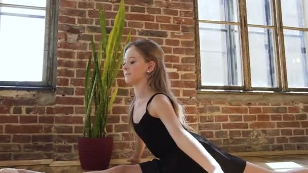 Aantrekkelijk meisje doet uitrekken zich zittend op een vloer. Aantrekkelijke jonge ballerina in een zwarte tutu is betrokken bij het uitrekken. Sporten in de fitnessruimte, ballroom en ballet school — Stockvideo