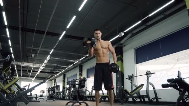 Atractivo chico deportivo haciendo ejercicio con pesas en el gimnasio . — Vídeo de stock